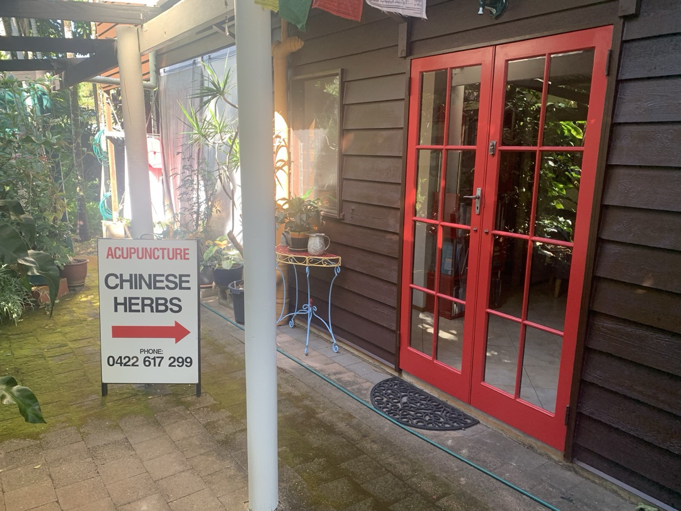The clinic’s red-framed French door entrance, tucked among tropical garden plants