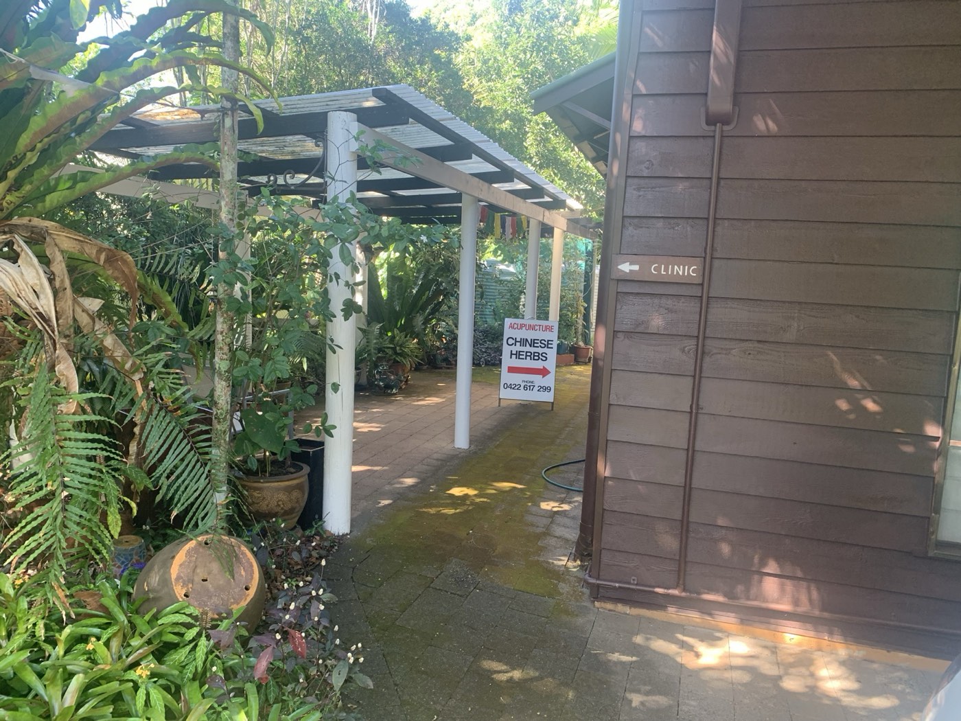 Garden pergola walkway leading to the clinic, with a "Clinic" directional sign on the wall